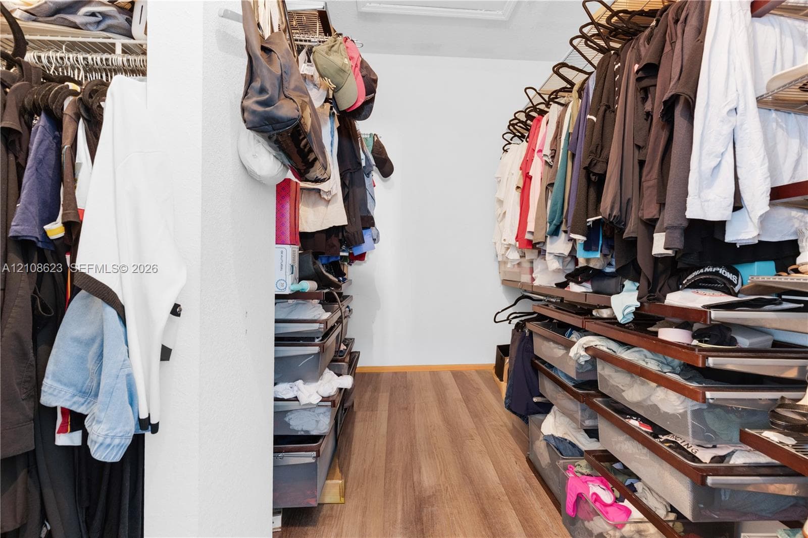 Walk-in closet featuring multi-tiered hanging rods, built-in drawer storage, overhead shelving, and wood-finish flooring