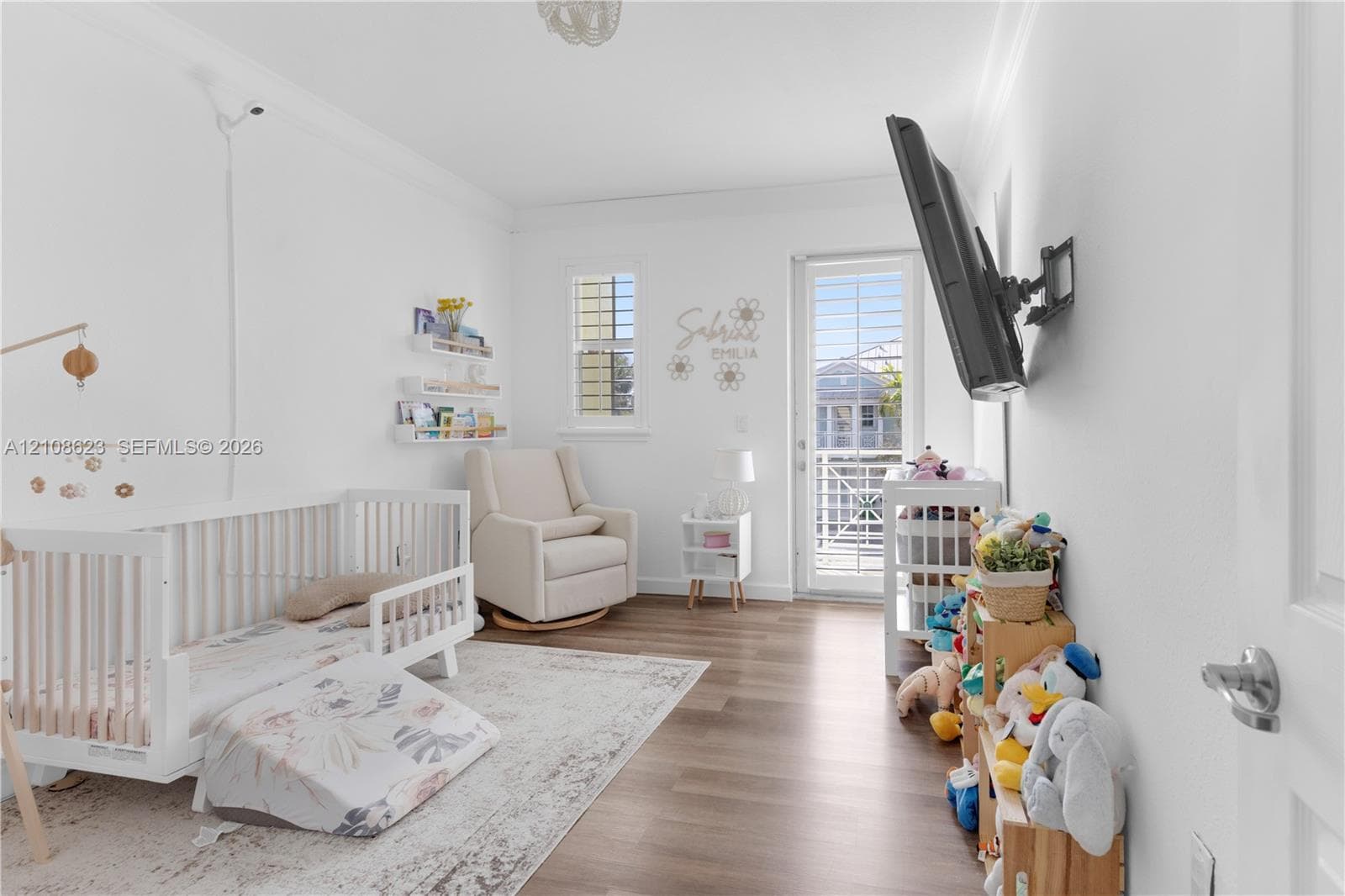 Room featuring wood-finish flooring, crown molding, built-in shelving, and a glass-paned door
