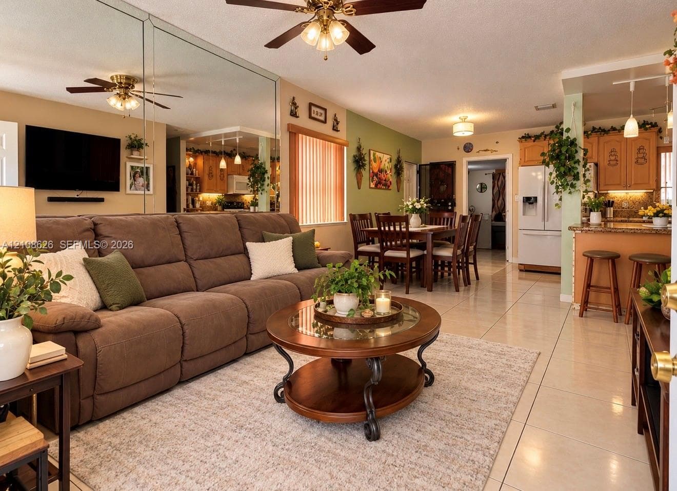 Open-concept living and dining area featuring large-format tile flooring, mirrored wall accent, breakfast bar with pendant lighting, and built-in wooden cabinetry