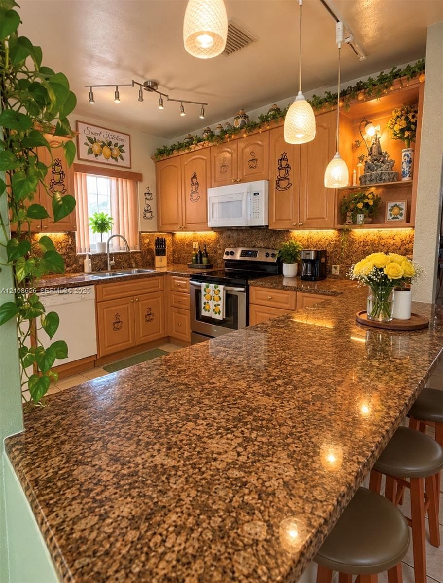 Kitchen featuring stone countertops, custom wood cabinetry, stainless steel appliances, tiered pendant lighting, and under-cabinet illumination