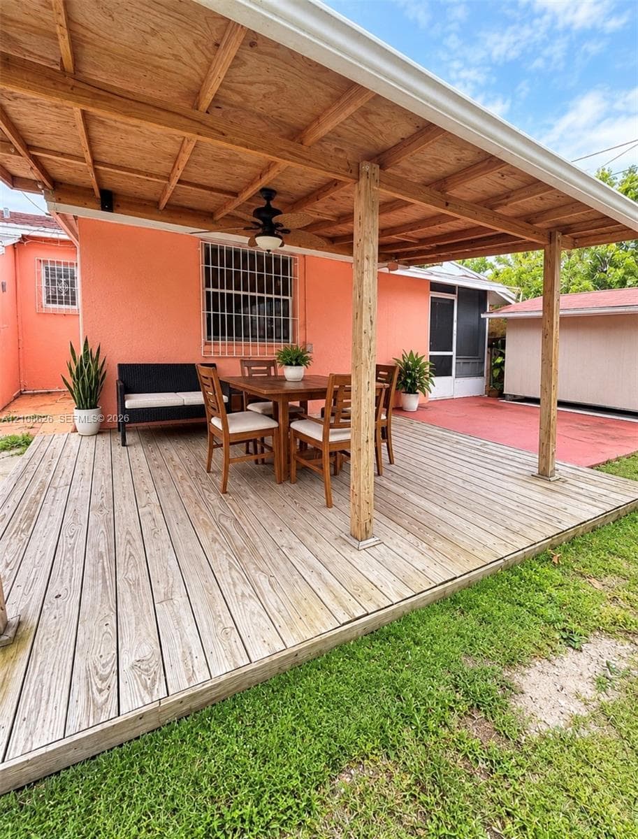 Covered wood deck featuring a ceiling-mounted fan, wood-beam supports, and metal security bars on exterior windows