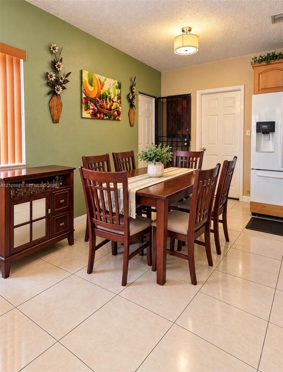 Dining area featuring polished light-toned floor tiles, a drum-style ceiling light fixture, wood cabinetry, and vertical blind window treatments