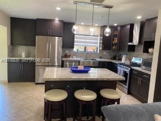 Kitchen featuring dark-toned cabinetry, stainless steel appliances, stone-surface countertops, central island, and ceramic tile flooring