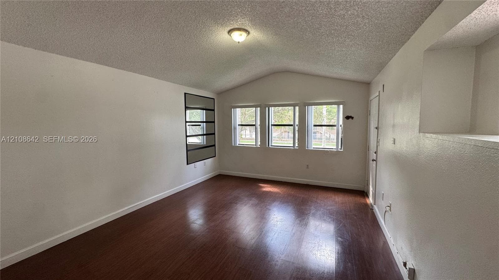 Vaulted ceilings, wood-finish flooring, three windows with natural light, and recessed shelving