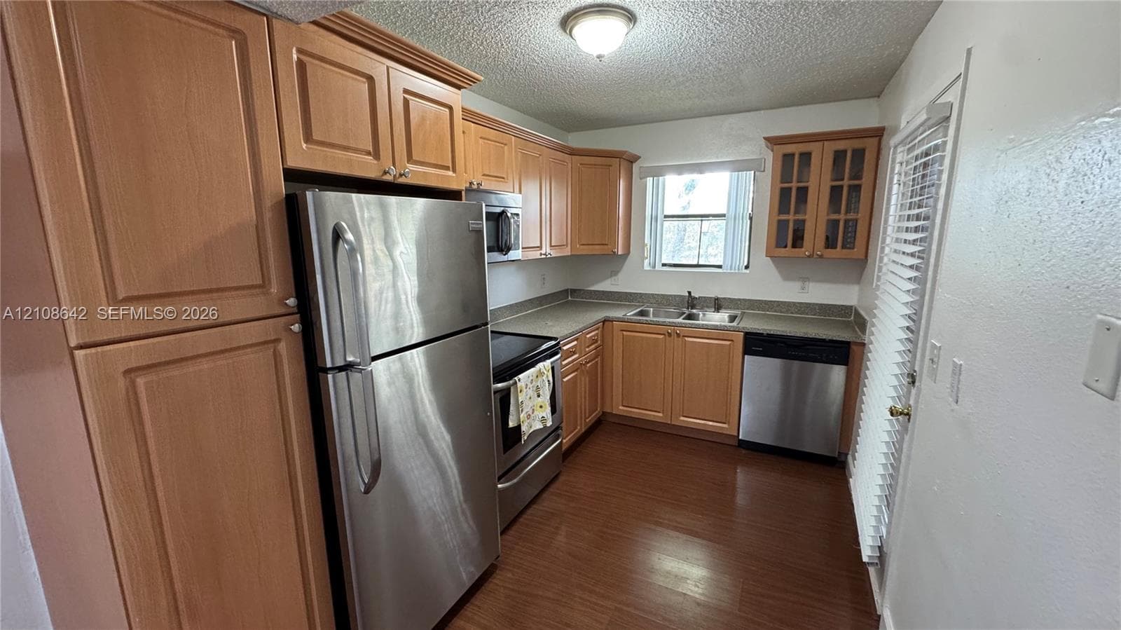 Kitchen featuring wood cabinetry, stainless steel appliances, dual-basin sink, and wood-finish flooring