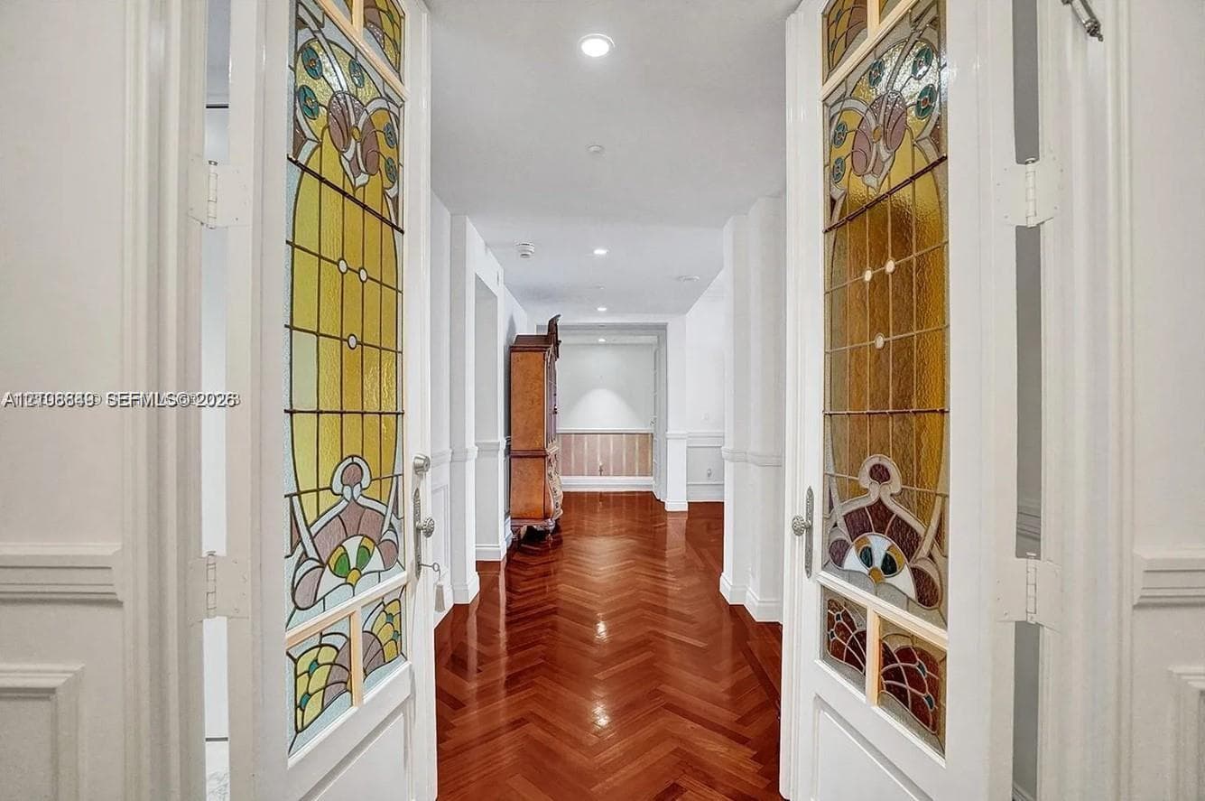 Double doors featuring decorative stained-glass panels, wood-finish flooring laid in a herringbone pattern, wainscoting, and recessed ceiling lighting