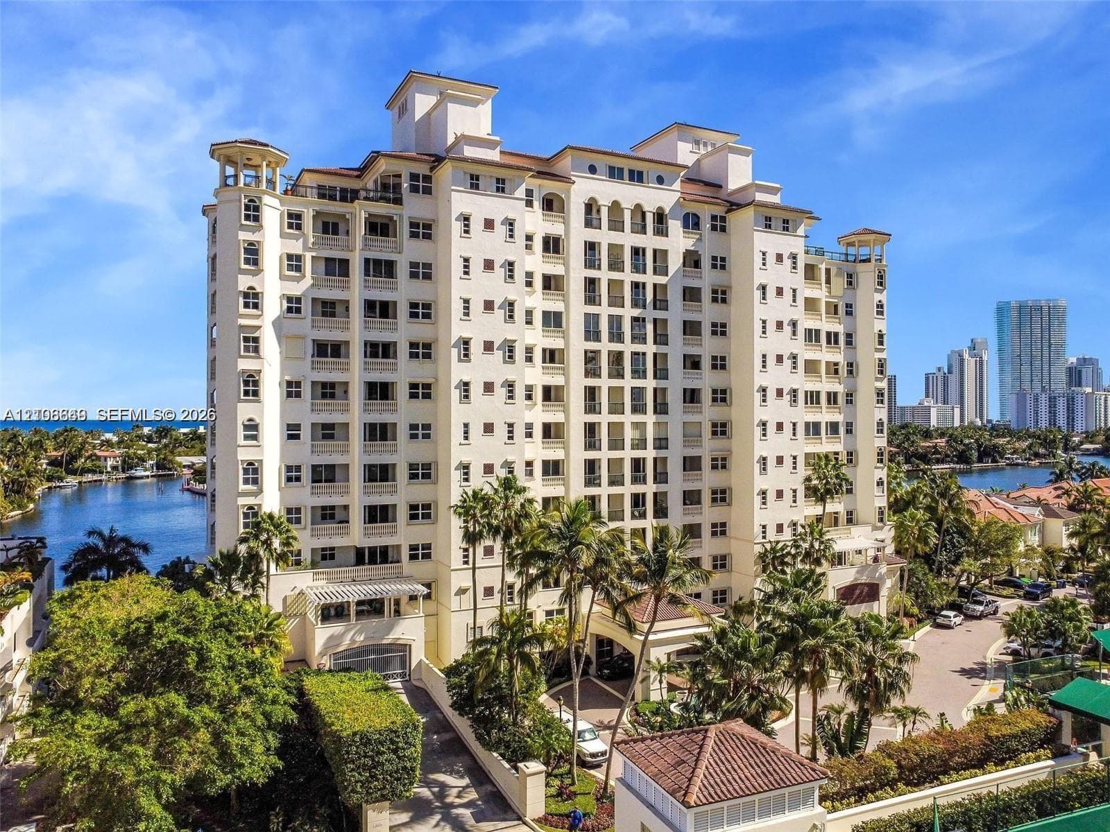 Mid-rise waterfront high-rise building featuring multi-level balconies, arched architectural detailing, a clay tile roof, and porte-cochère entry