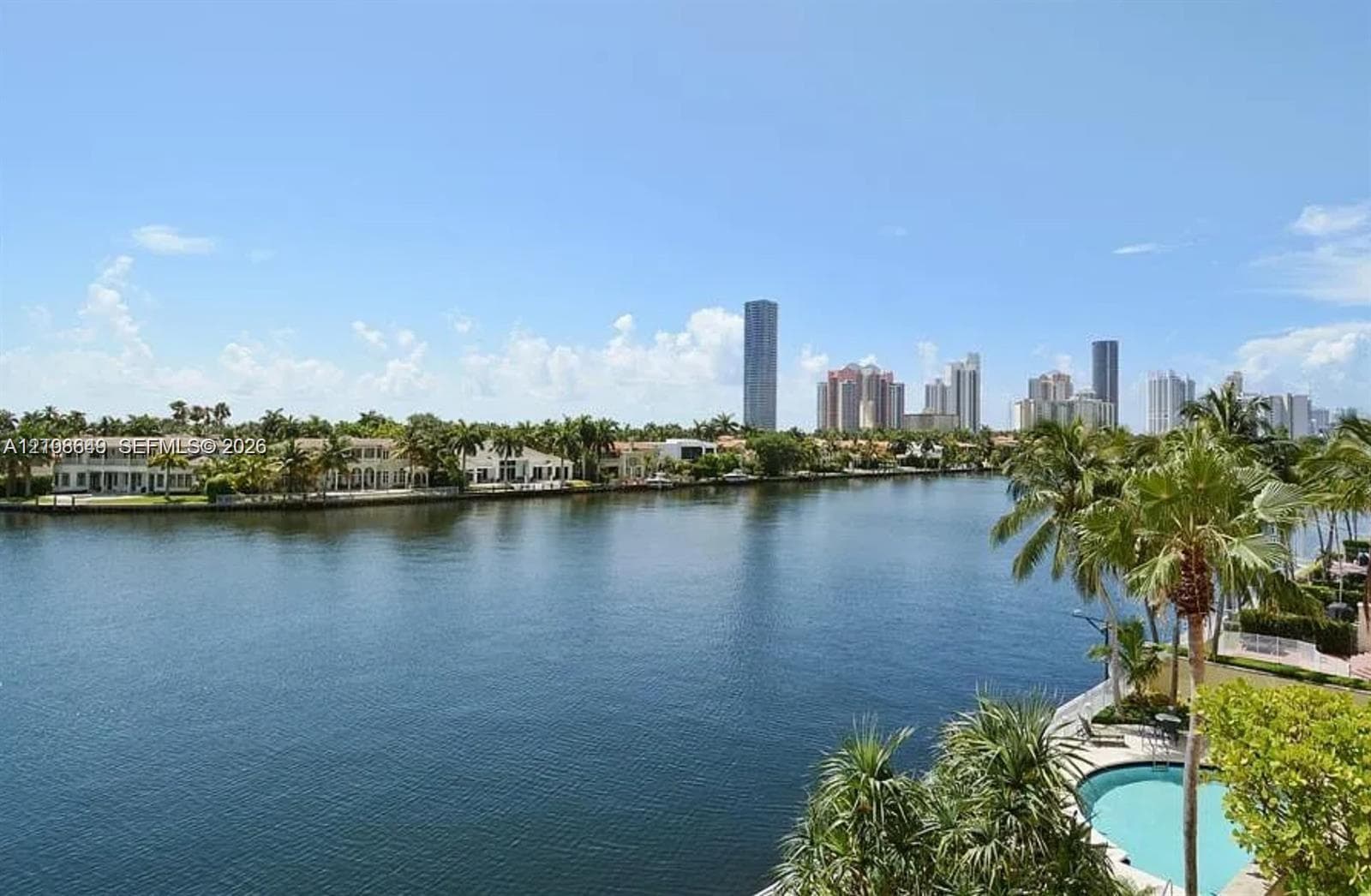 Waterfront property featuring a canal, private swimming pool, mature palm trees, and coastal skyline horizon