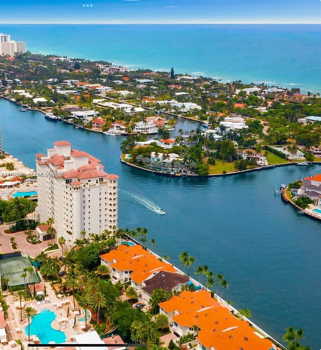 Aerial perspective featuring waterfront residential structures, multi-story building, swimming pool, tennis court, and canal access