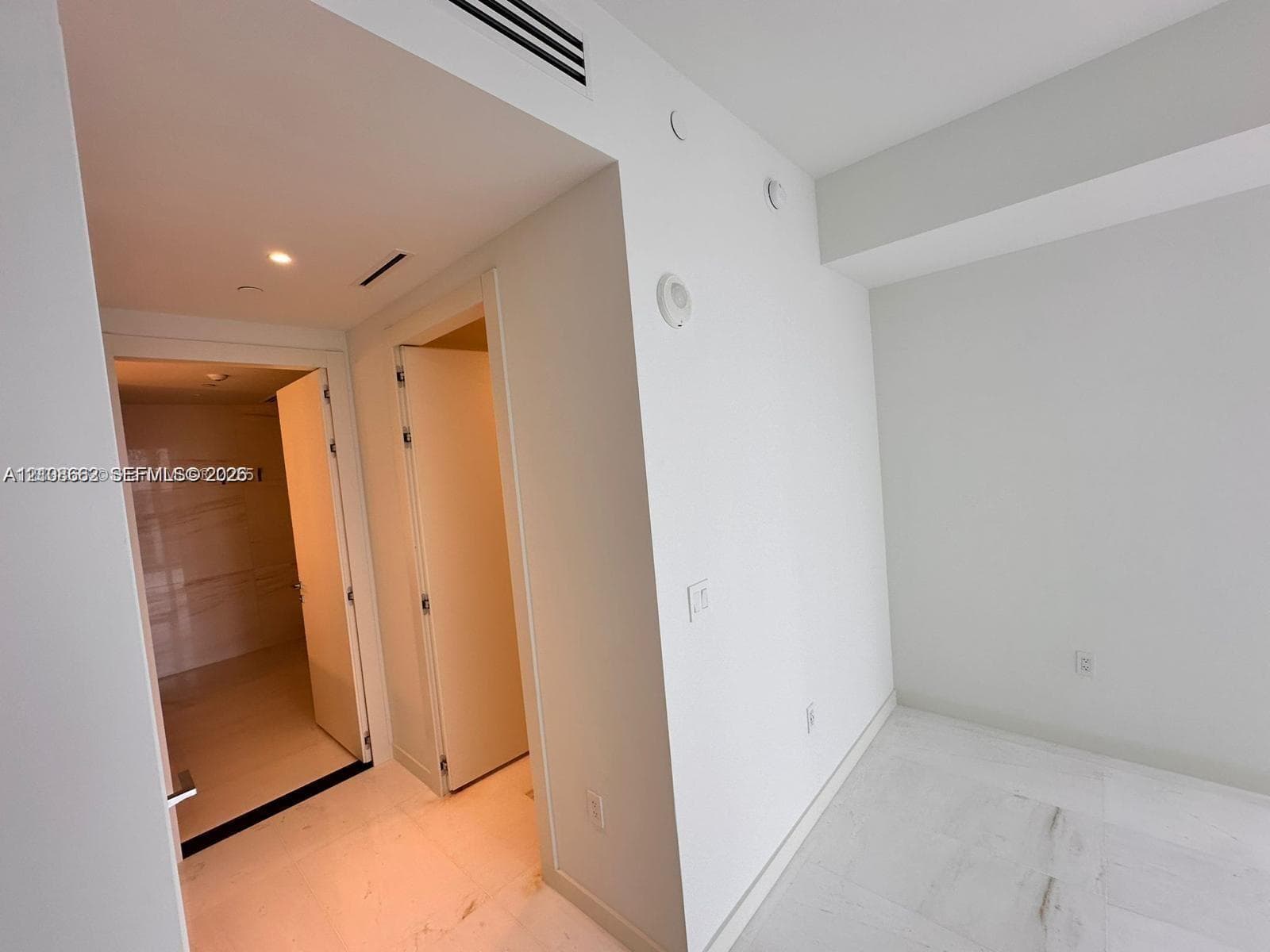 Interior space featuring white stone-finish flooring, recessed ceiling lighting, and smooth-finish walls with minimalist door frames