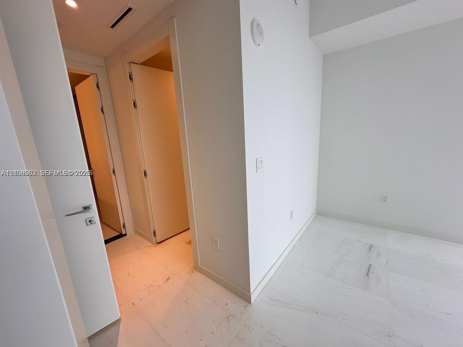 Interior space featuring white stone-finish flooring, recessed lighting, and solid-core doors with contemporary brushed-metal hardware