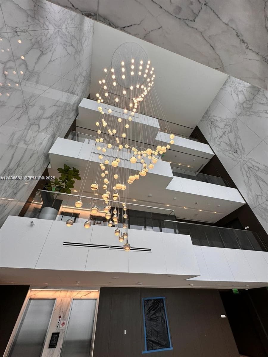 Multi-story atrium featuring full-height stone cladding, a tiered geometric balcony design, glass railings, and an expansive multi-globe pendant light fixture