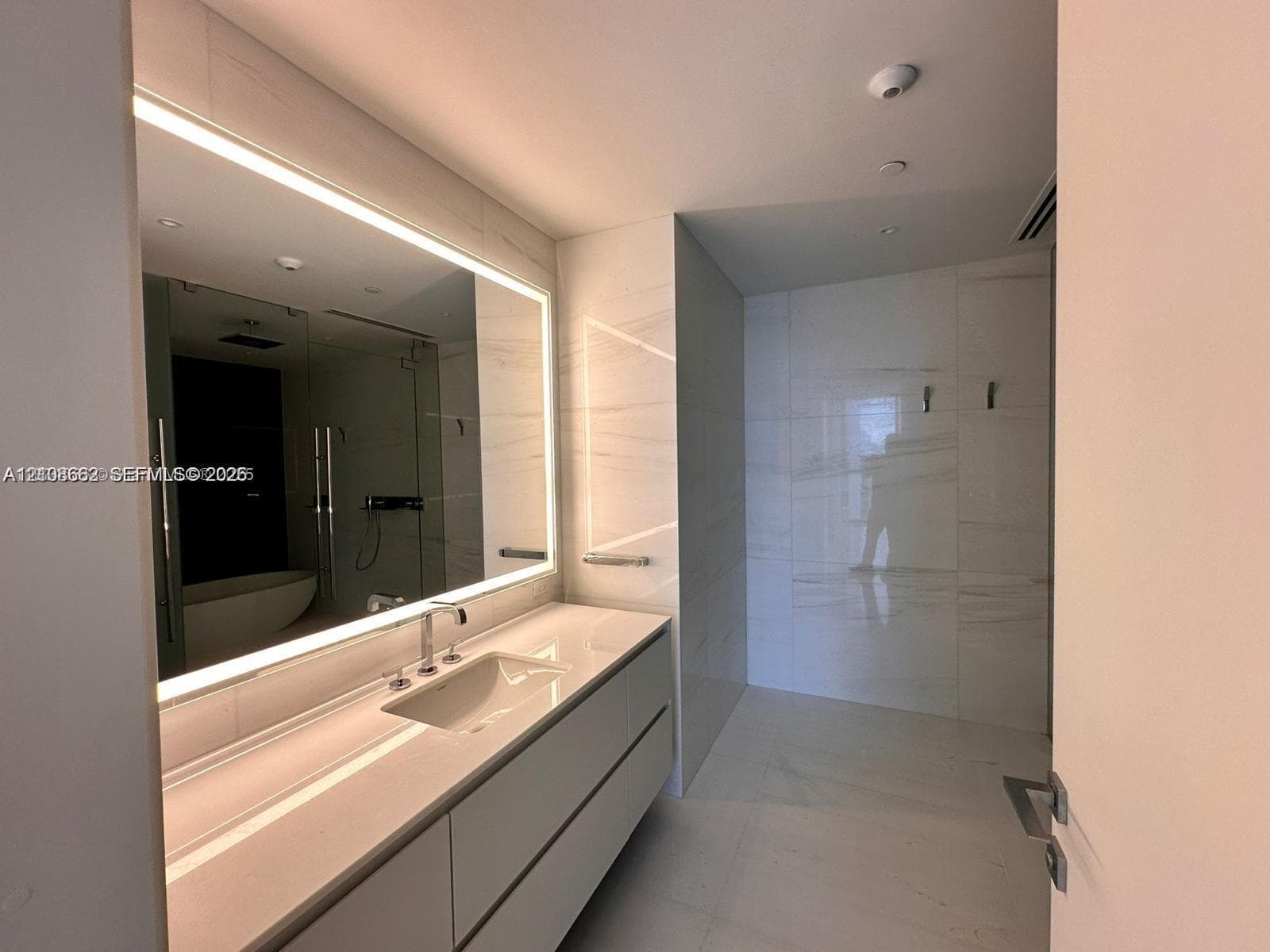 Wall-mounted floating vanity with integrated countertop sink, large LED-backlit mirror, and extensive large-format tile wall cladding