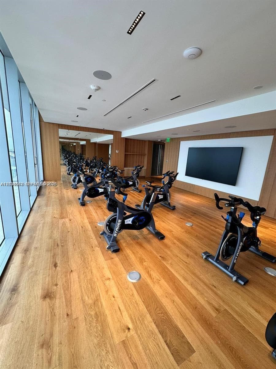 Fitness room featuring floor-to-ceiling windows, wood-finish flooring, full-wall mirrors, recessed lighting, and integrated wall-mounted display