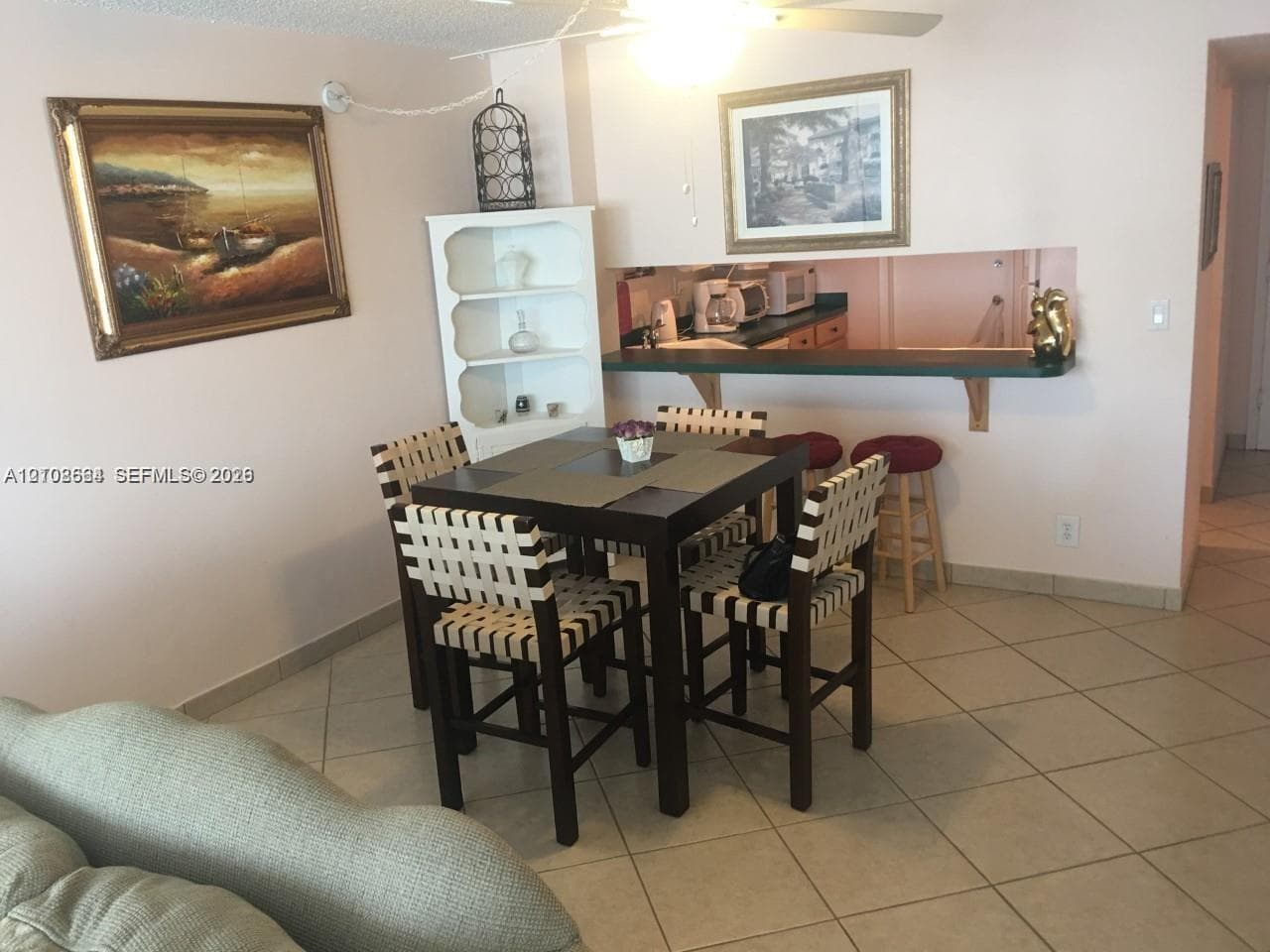 Open-concept interior featuring light-toned tile flooring, built-in shelving, a kitchen pass-through counter, and a ceiling fan