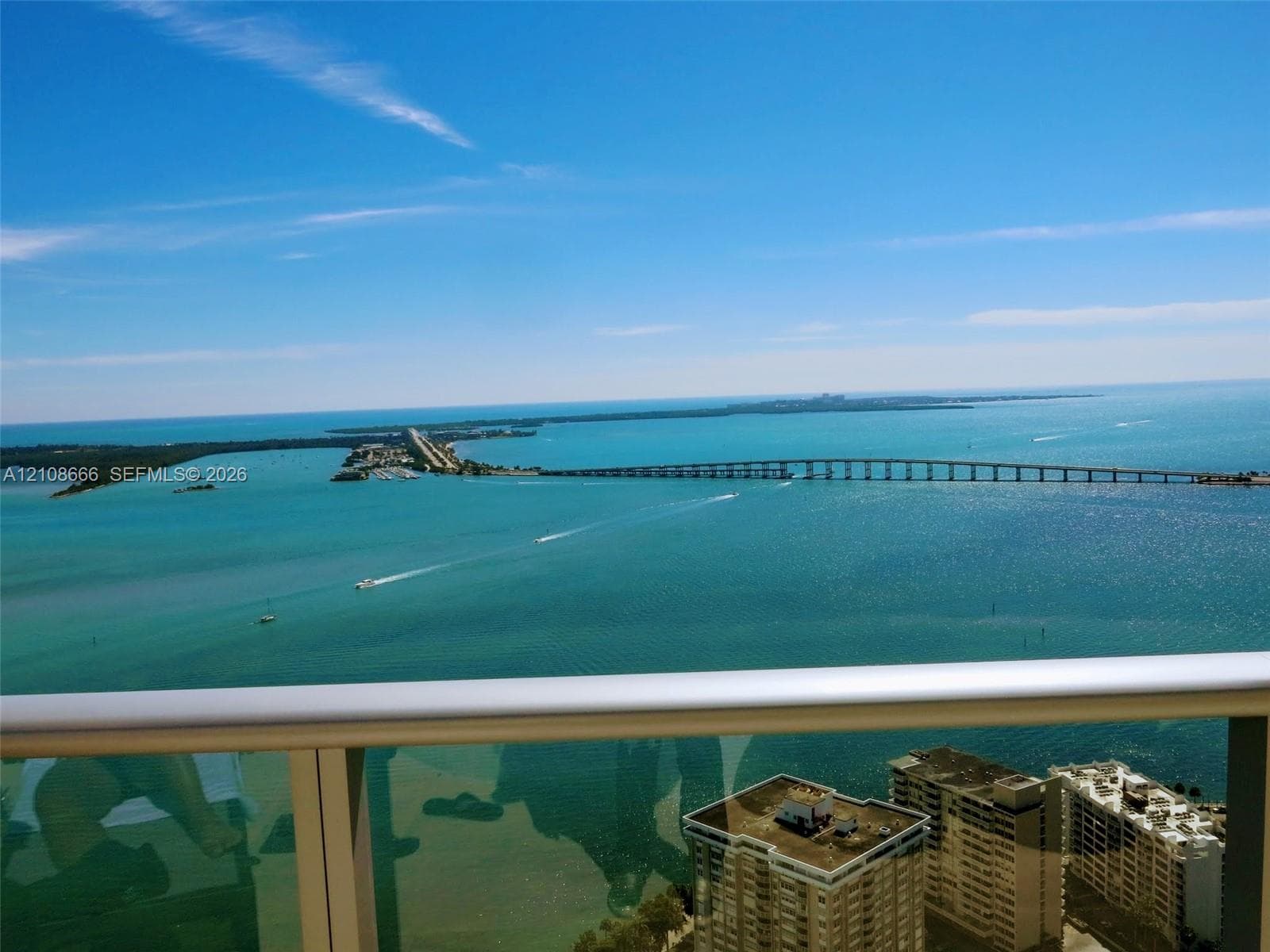 High-rise balcony featuring a metal railing with glass panels, showcasing panoramic coastal scenery, open water, and a bridge