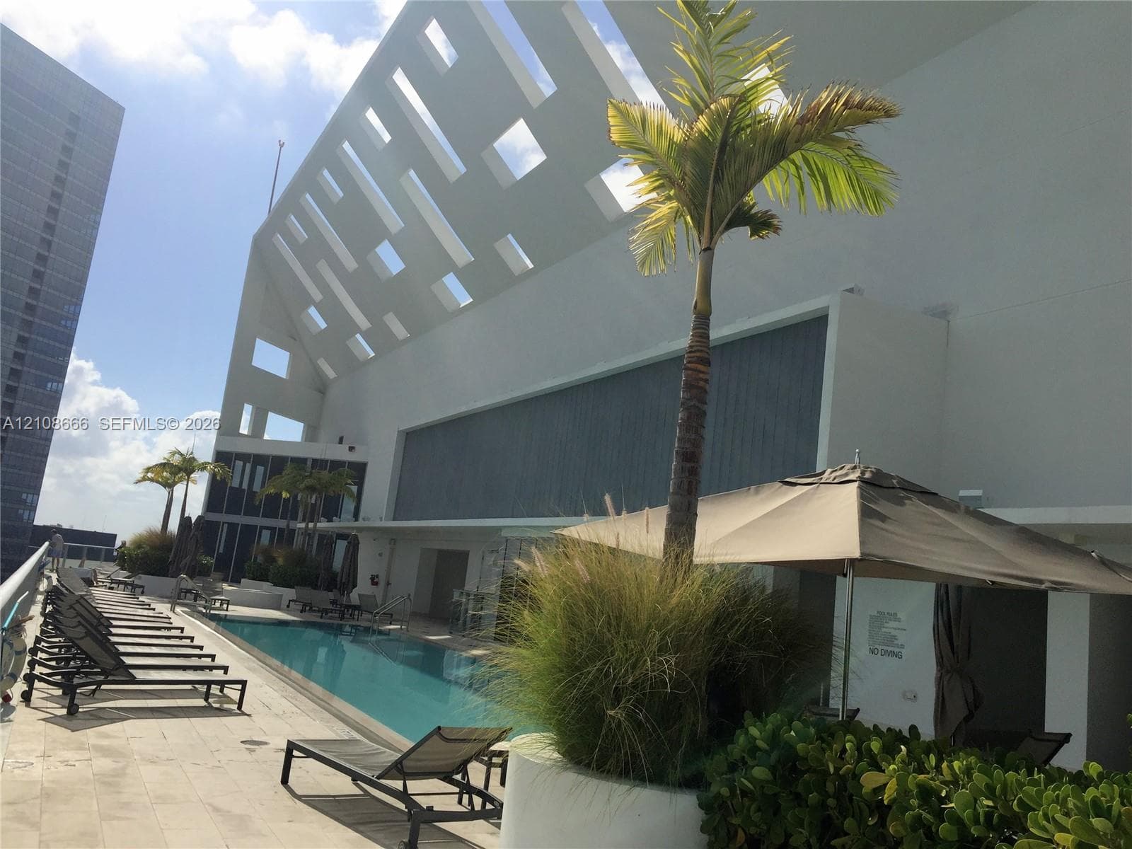 Rooftop swimming pool featuring a concrete deck, architectural geometric screening, and integrated landscaping planters