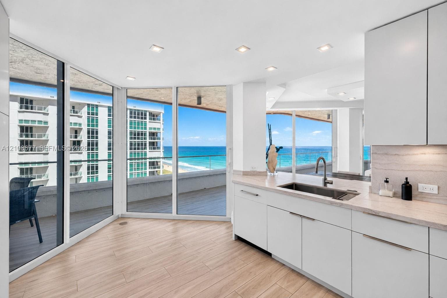 Kitchen featuring flat-panel white cabinets, stone counters, undermount sink with a beautiful gooseneck faucet, wood look plank porcelain flooring, and floor-to-ceiling windows with balcony access for morning sunrise breakfast.