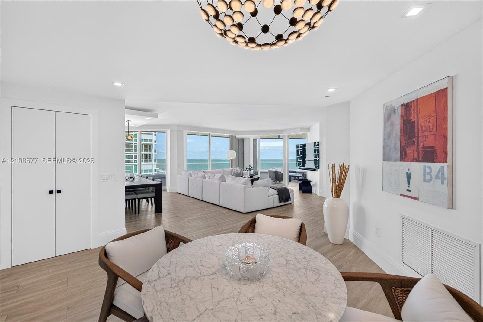 Open-concept informal dining or office space featuring wood look plank porcelain flooring, views toward the living room area, floor-to-ceiling windows, recessed lighting, and a beautiful oversized decorative chandelier