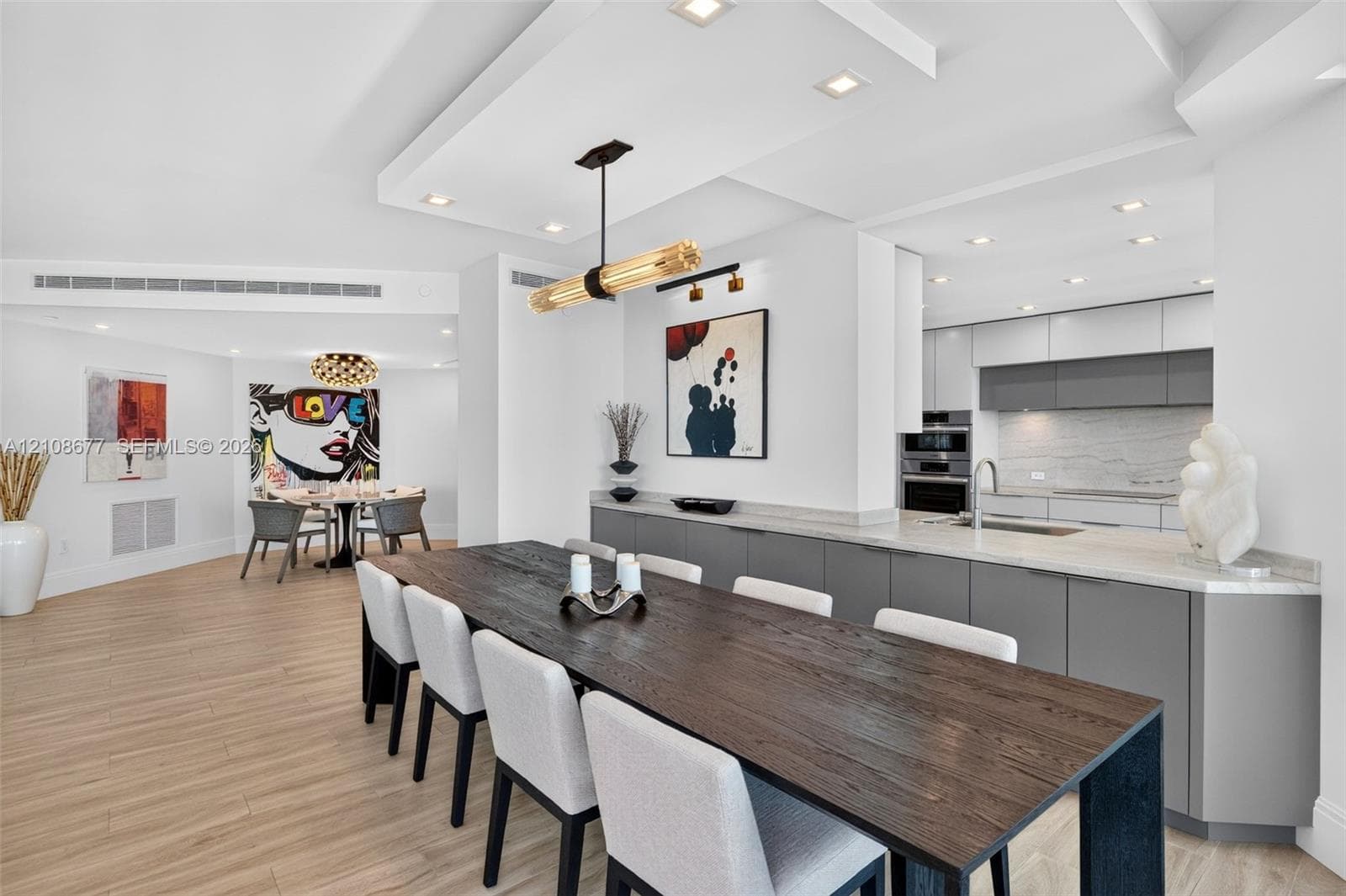 Open-concept dining space space featuring wood look plank porcelain flooring, a coffered ceiling with recessed lighting, minimalist flat-panel cabinets, stone counters, and a beautiful modern pendant fixture. Great open pass through to the kitchen and sink, amazing buffet / storage space