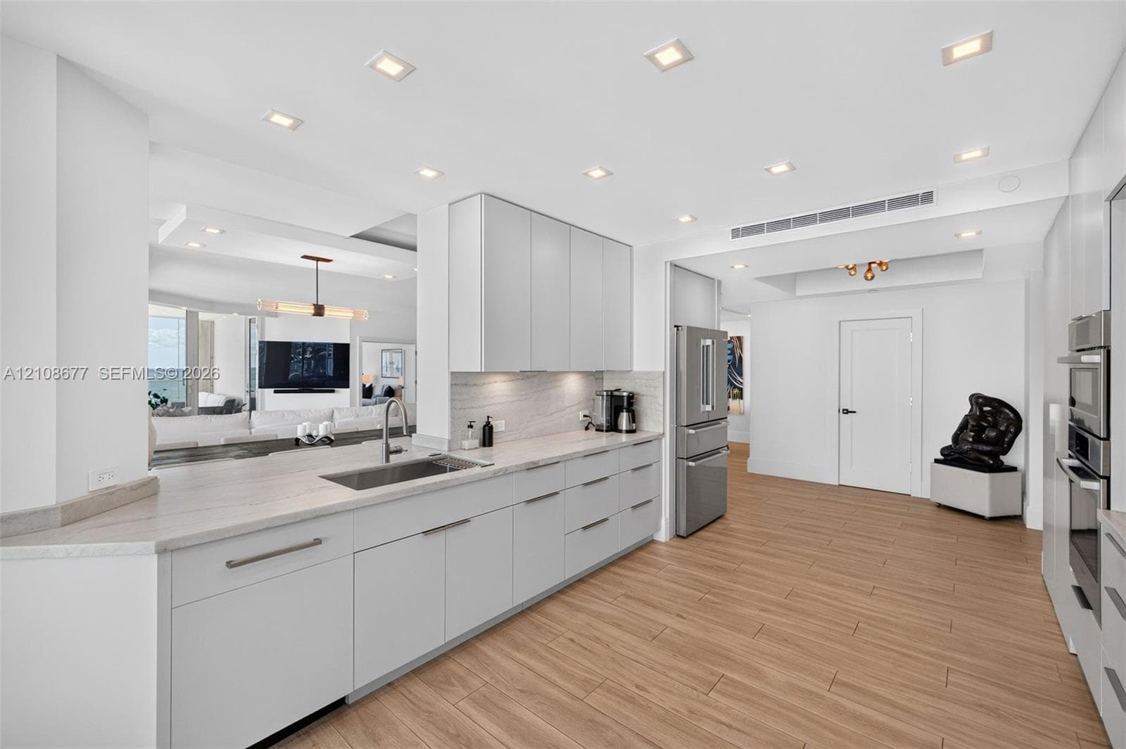 Kitchen featuring flat-panel cabinets, light-toned stone counters, stainless appliances including a wall ovens, recessed lighting, and wood look plank porcelain flooring - pass through to dining area and buffett / serving area