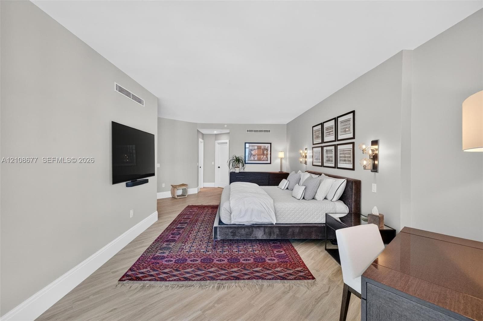 Spacious room featuring wood look plank porcelain flooring, neutral wall tones, and wall-mounted light fixtures. View toard primary bathroom and large walk in closet