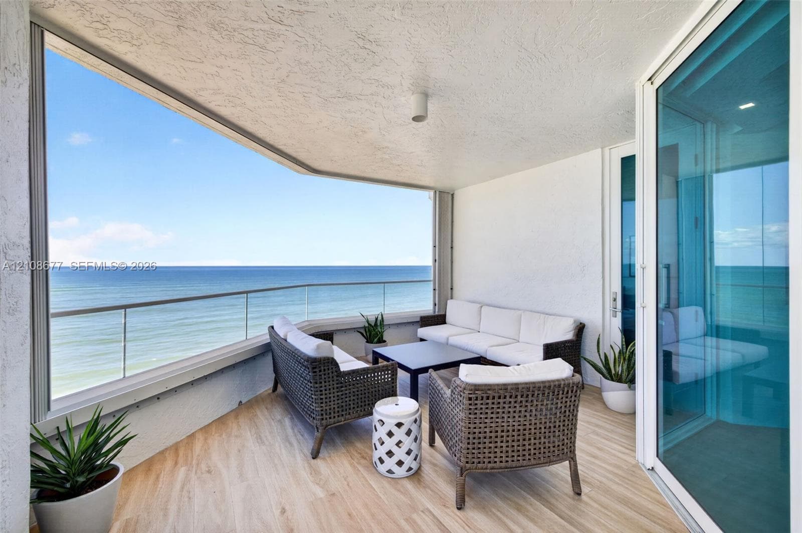 Covered balcony featuring the same wood look plank porcelain  flooring as interior, a frameless glass railing, and expansive ocean scenery. Additional protection for your furniture with upgraded accordion shutters.