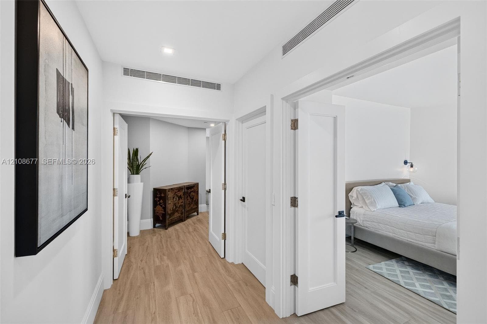 Hallway toward primary bedroom w/ double door entry, w/ wood look plank porcelain flooring, recessed lighting, and solid-core doors with matte black hardware, one guest bedroom to the right, with a laundry room separating the two rooms (door closed)
