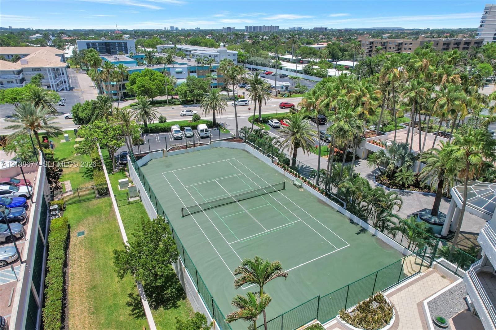Aerial perspective of a coastal high-rise property featuring direct beach access, multiple outdoor swimming pools, manicured green space, and mature tropical landscaping