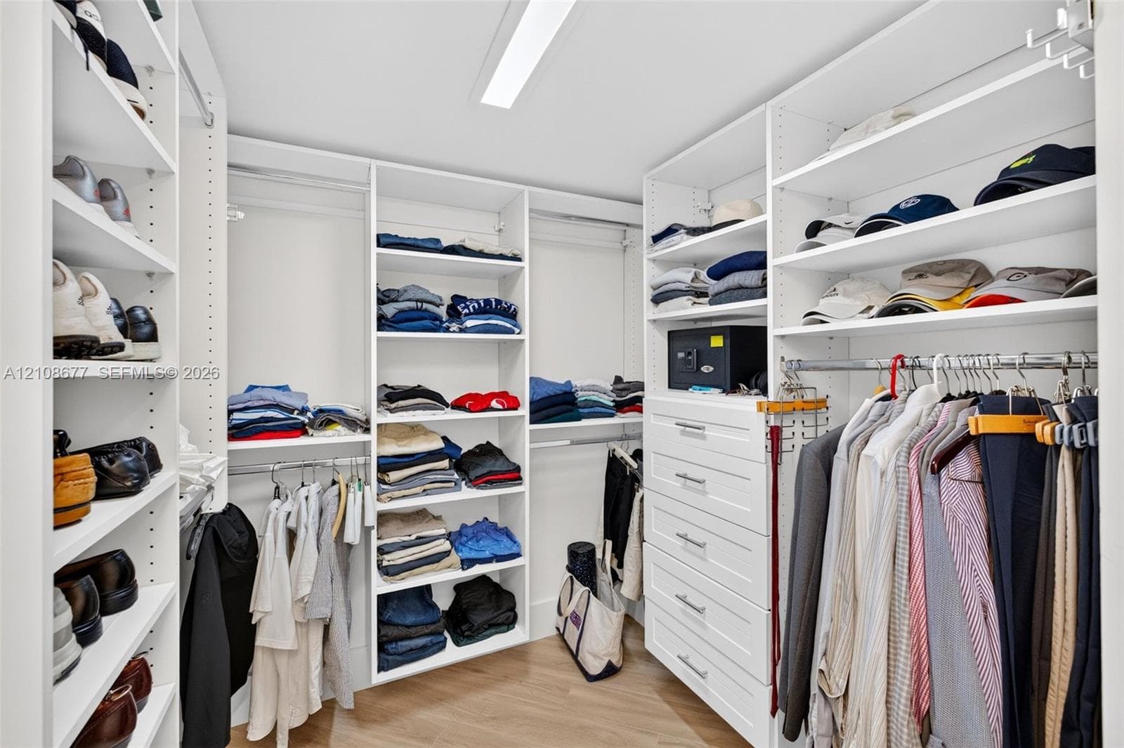 View toward shorter side of the custom walk-in closet featuring floor-to-ceiling white shelving, integrated clothing rods, stacked drawer storage, and wood look plank porcelain flooring