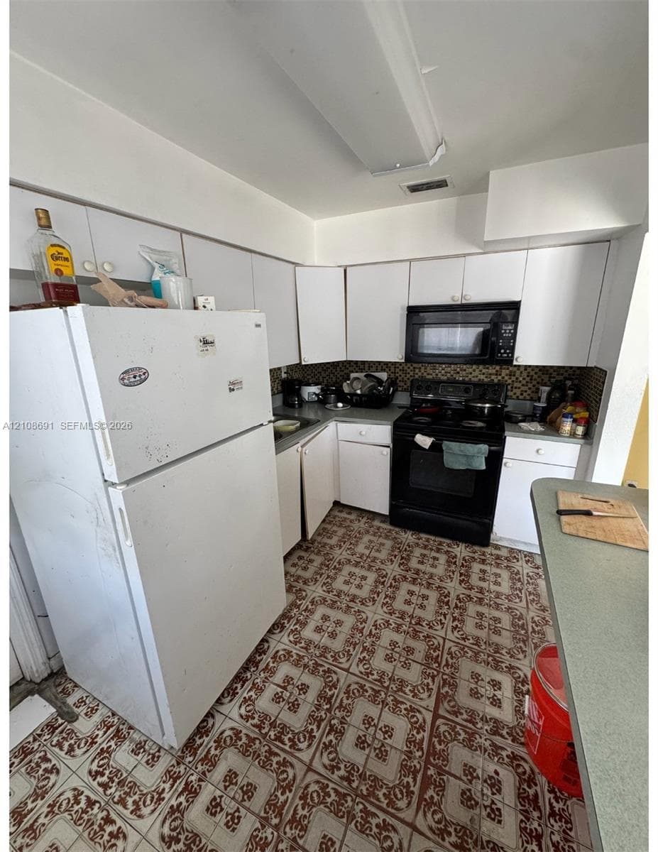 Kitchen featuring white cabinetry, patterned tile flooring, an integrated microwave, and a black range