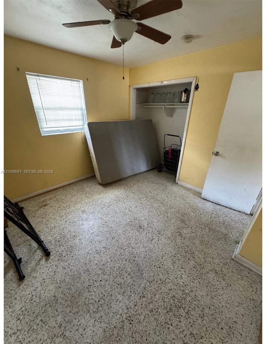 Interior space featuring terrazzo flooring, a ceiling fan with light fixture, a single-hung window with blinds, and a built-in closet with shelving