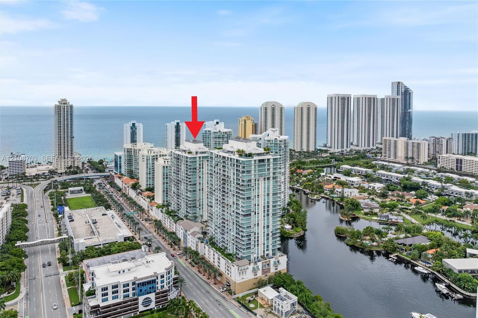 Aerial perspective of a high-rise residential building featuring floor-to-ceiling glass windows, multiple private balconies, and a coastal location