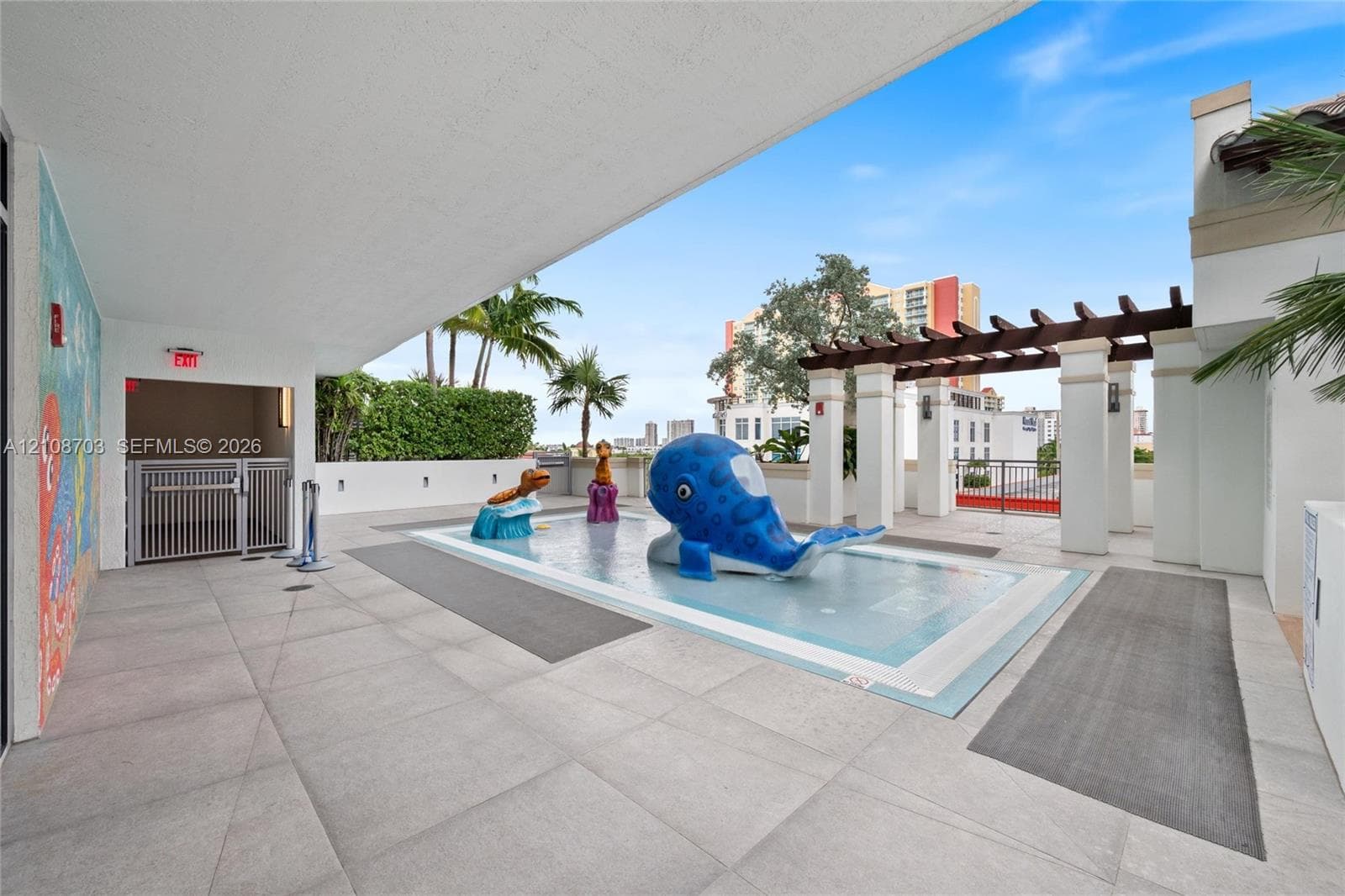 Splash pad featuring built-in water play structures, tile surround, stone-finish patio, and a covered timber pergola