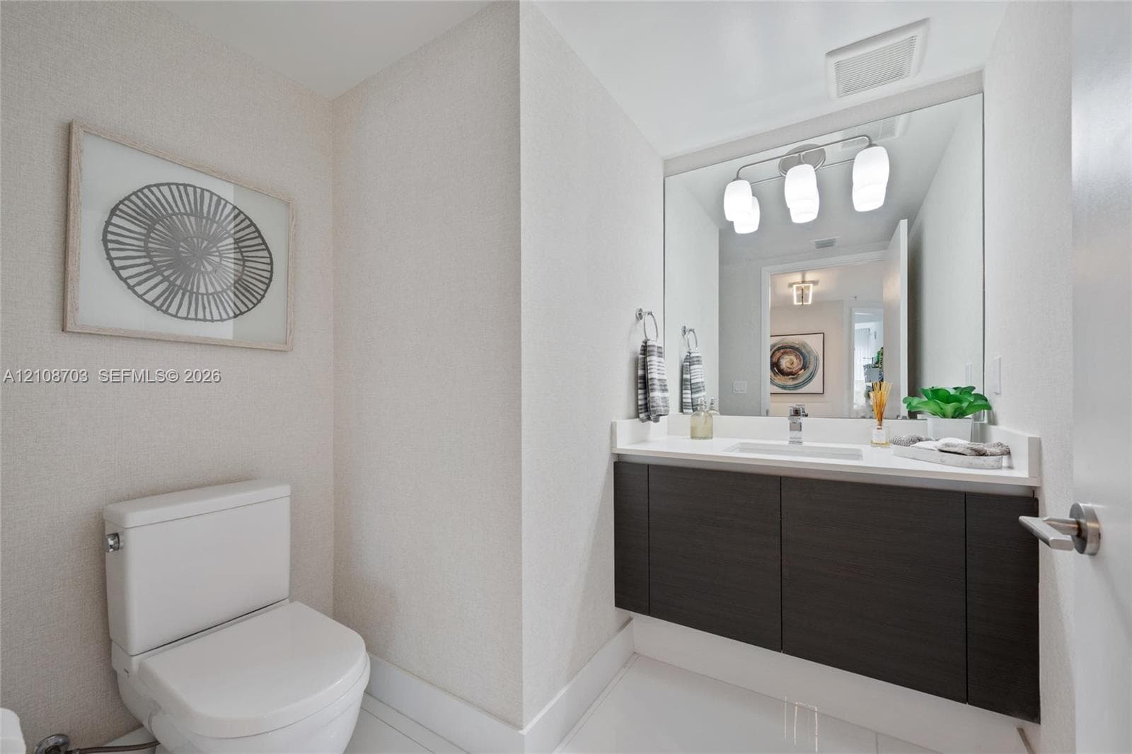 Wall-mounted floating vanity with dark wood-finish cabinetry, solid-surface countertop, rectangular undermount sink, and three-light integrated vanity fixture