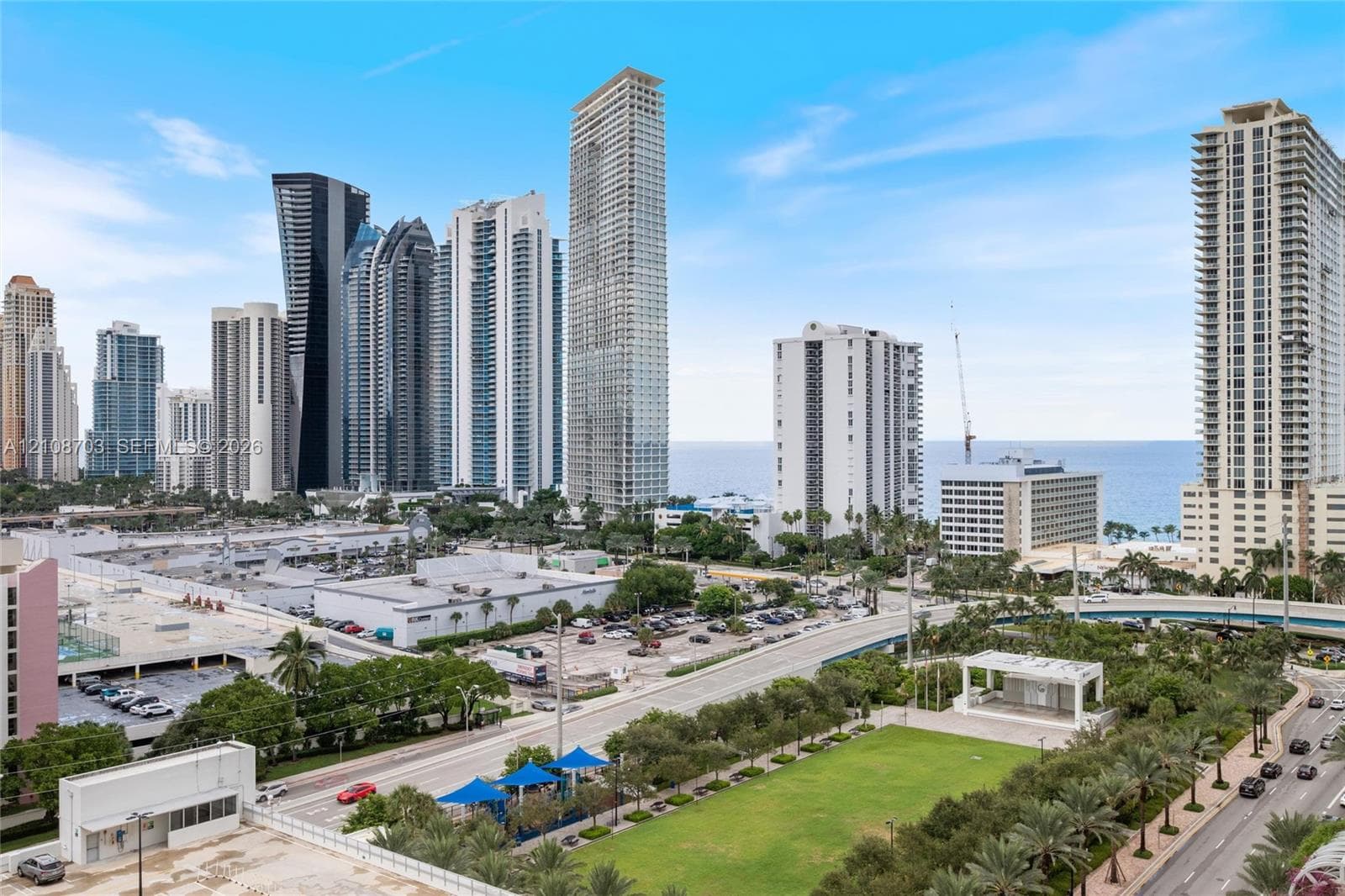 Urban landscape featuring high-rise buildings, a maintained green space with a pavilion, and coastal horizon