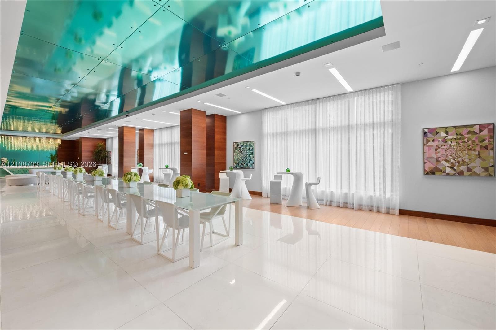 Large-format polished tile flooring, reflective blue-tinted ceiling paneling, floor-to-ceiling windows with integrated drapery, wood-finish wall paneling, and recessed linear lighting