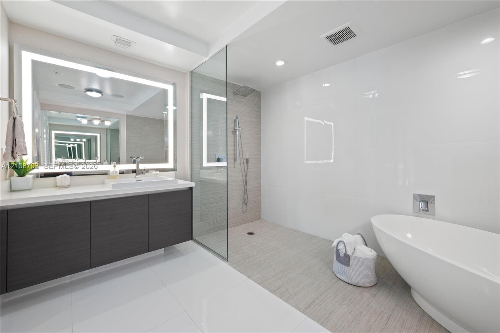 Floating vanity with rectangular vessel sink, frameless glass-enclosed shower, wall-mounted shower fixture, backlit vanity mirror, and freestanding soaking tub