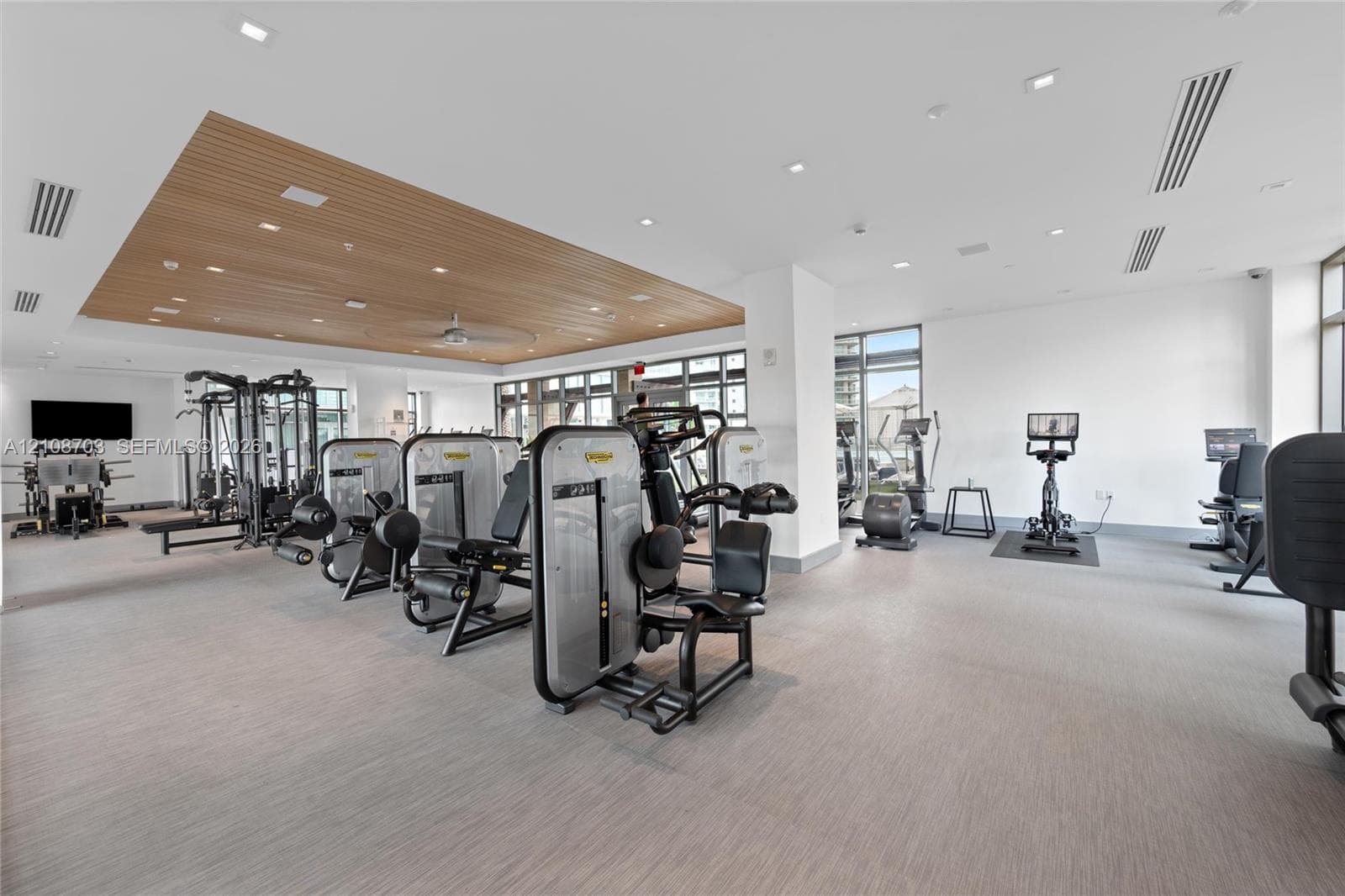 Fitness center featuring a recessed wood-paneled ceiling, integrated recessed lighting, neutral textured flooring, and large-format glass windows