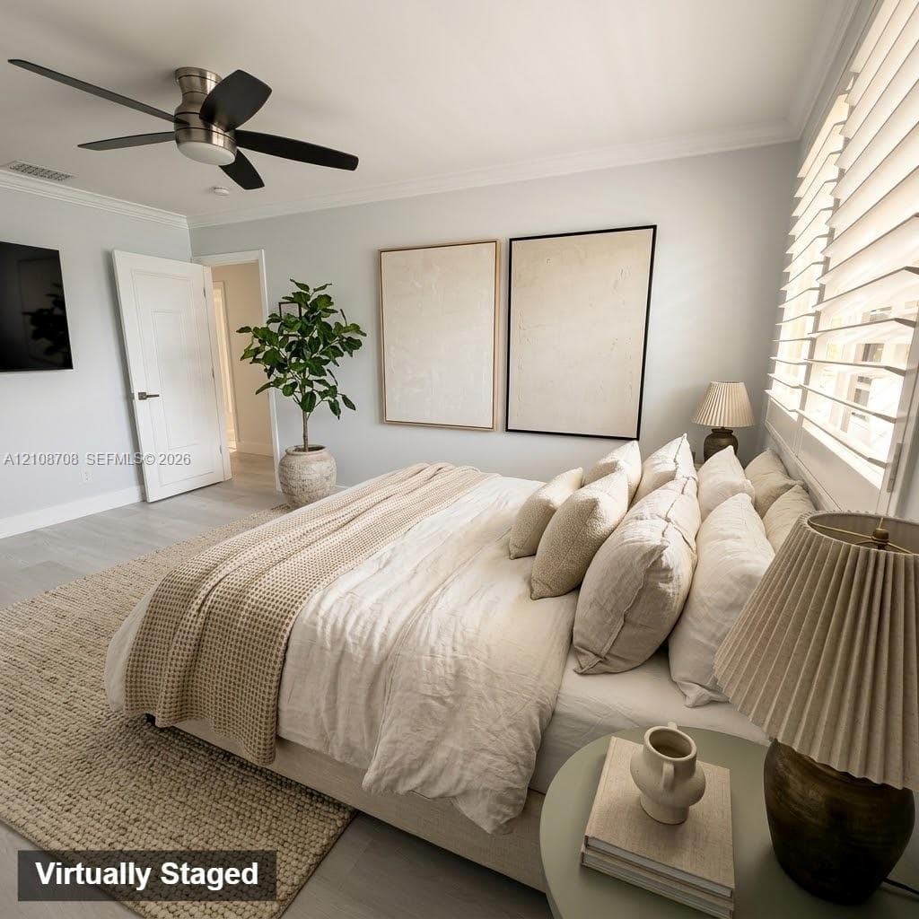 Light-toned wood-finish flooring, white paneled interior door, crown molding, and a five-blade ceiling fan with integrated lighting