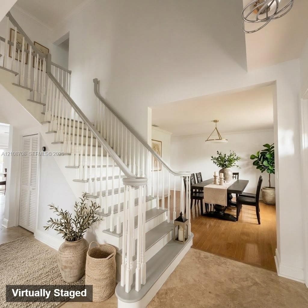 Staircase featuring painted wood treads, white balusters, and a matching handrail, set against high ceilings with a tiered geometric chandelier