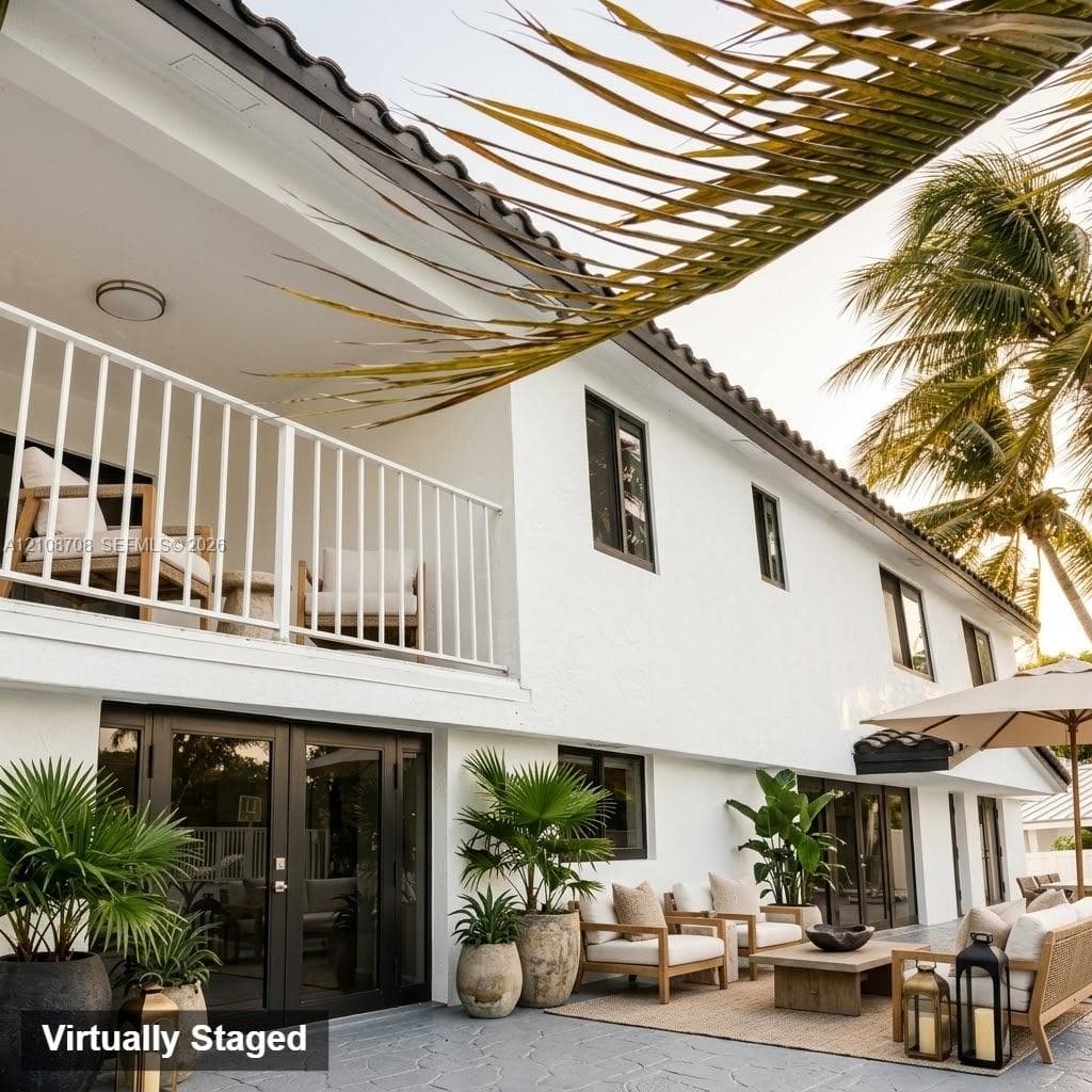 Two-story exterior featuring a white stucco finish, dark-trimmed windows, a tiled roof, a railed second-story balcony, and a paved patio area