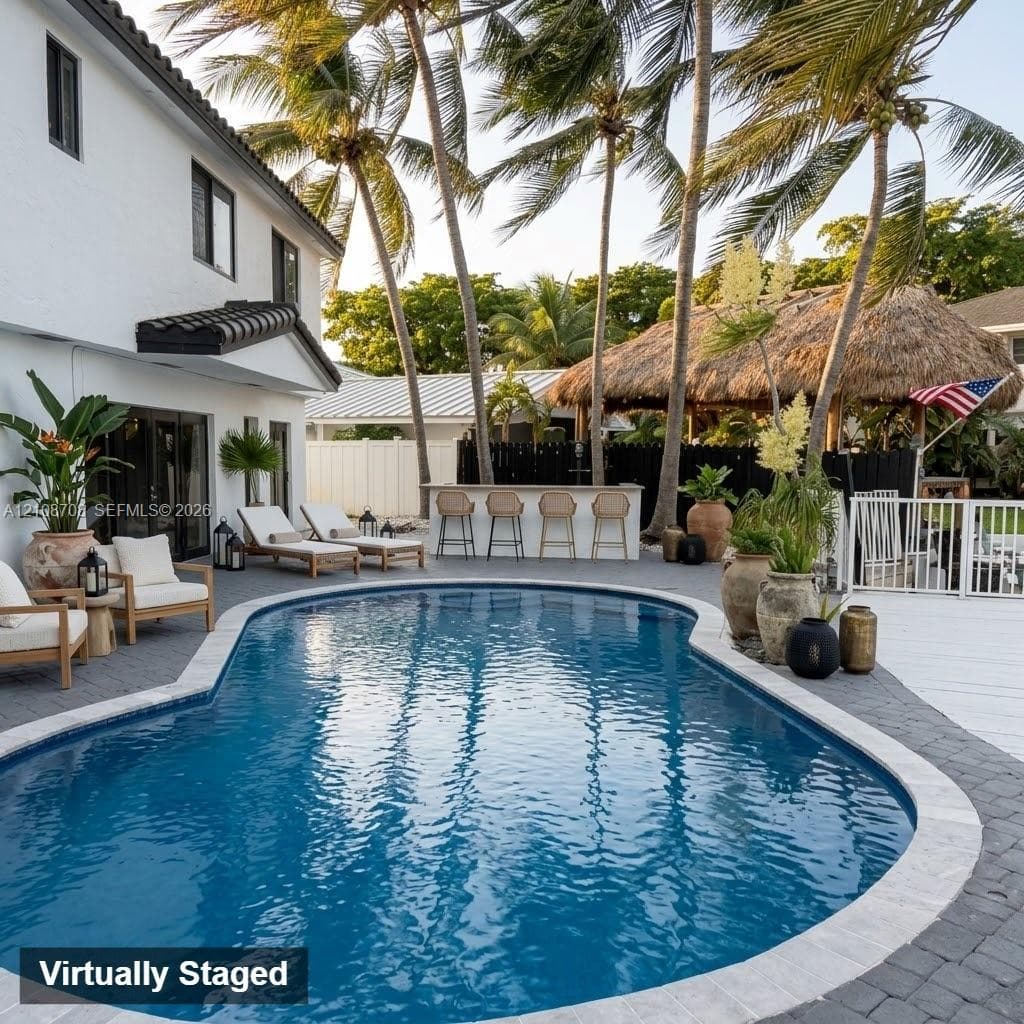 Custom pool with stone paver decking, integrated outdoor bar, and detached thatched-roof structure