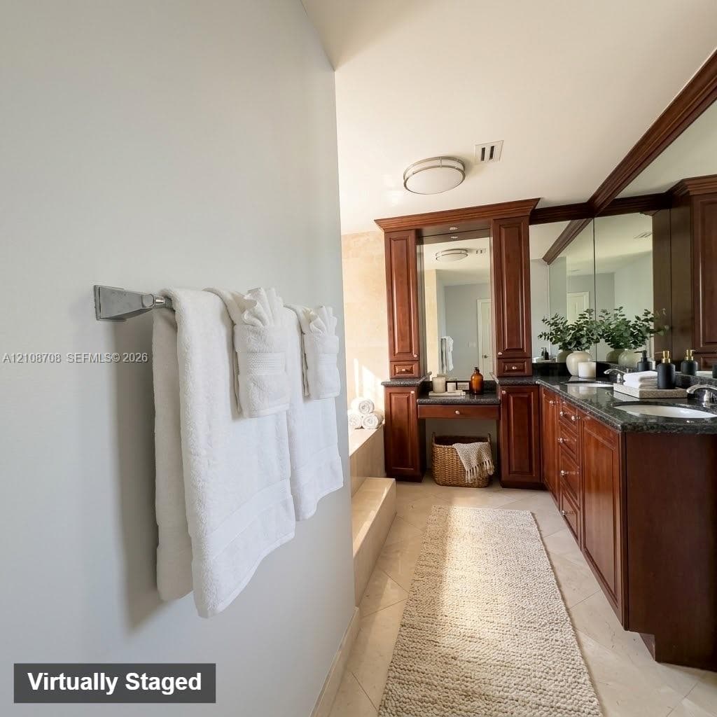 Custom wooden cabinetry featuring a seated vanity area, dark stone countertops, dual under-mount sinks, and large wall-mounted mirrors