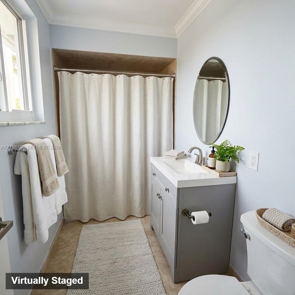 Bathroom featuring a gray shaker-style vanity with an integrated rectangular sink, crown molding, oval wall-mounted mirror, and a recessed shower area