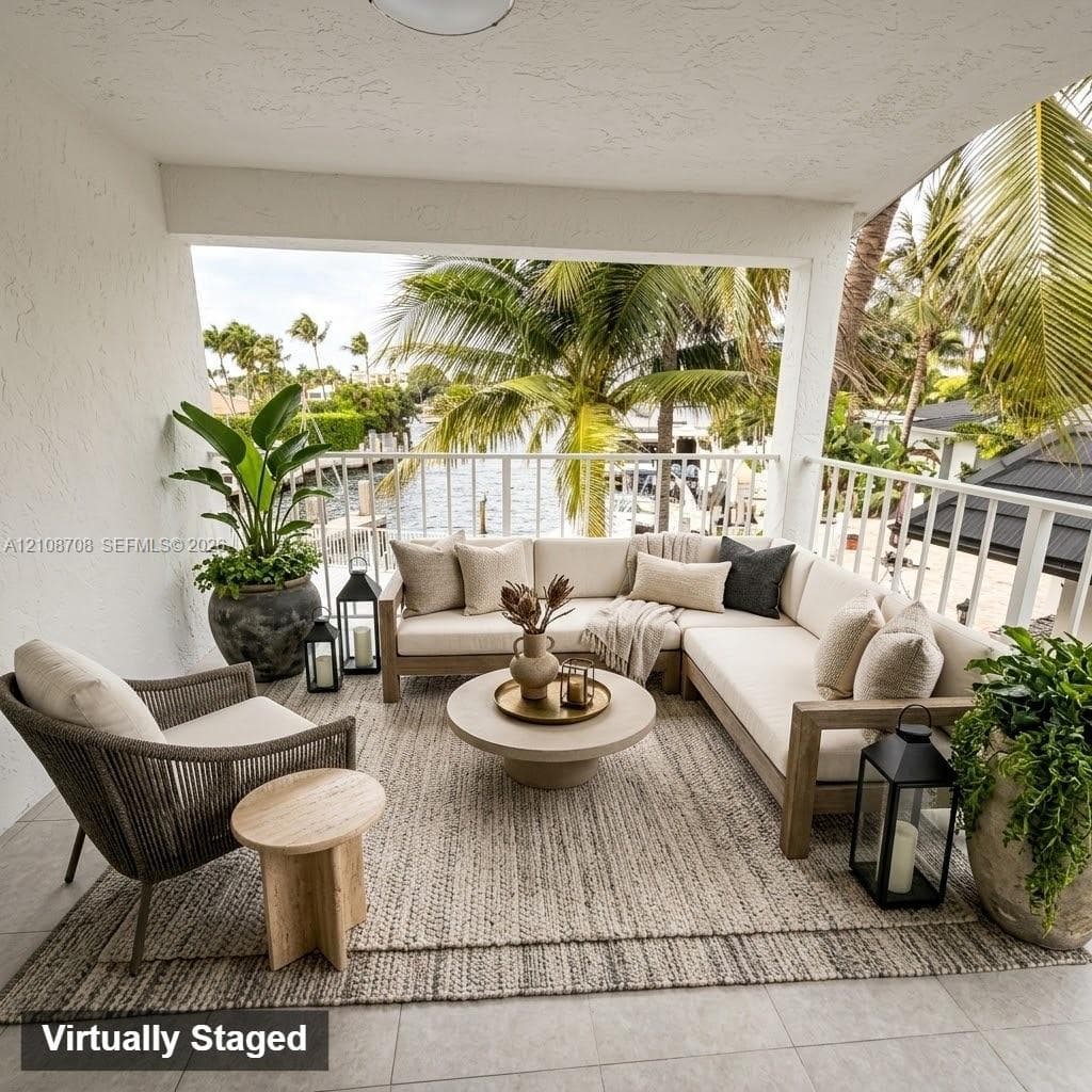 Covered outdoor balcony featuring light-toned tile flooring, white structural columns, and white railings overlooking a waterway