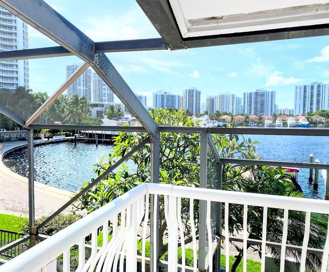 Enclosed balcony featuring a white metal railing, structural framing, and direct water exposure with a waterfront bulkhead