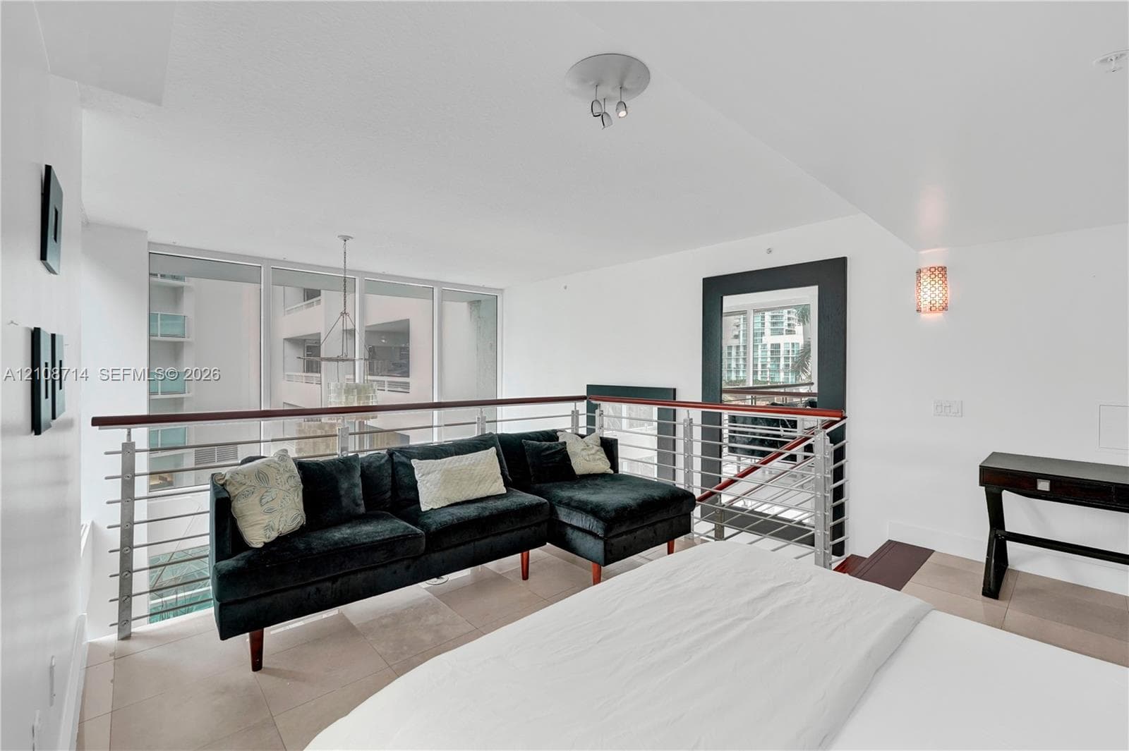 Open-concept mezzanine featuring metal horizontal-rail balustrades with a dark wood handrail, large floor-to-ceiling windows, tile flooring, and integrated wall-mounted lighting