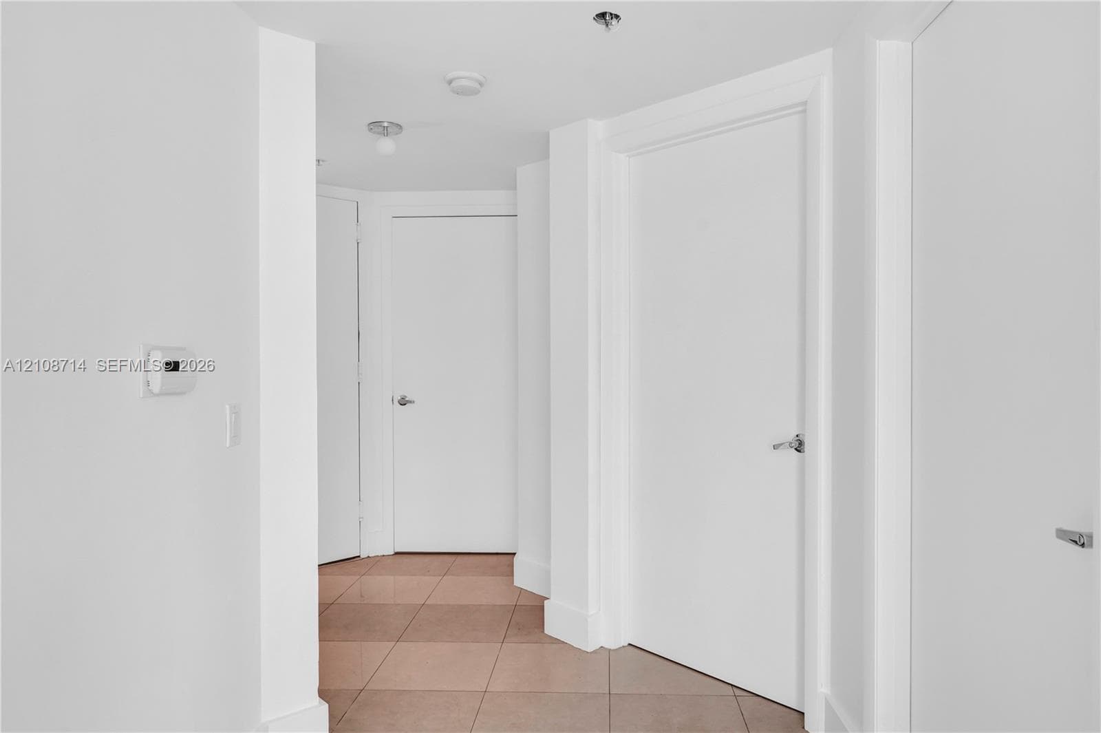 Interior hallway featuring neutral-toned tile flooring, solid core doors with brushed metal hardware, and recessed lighting