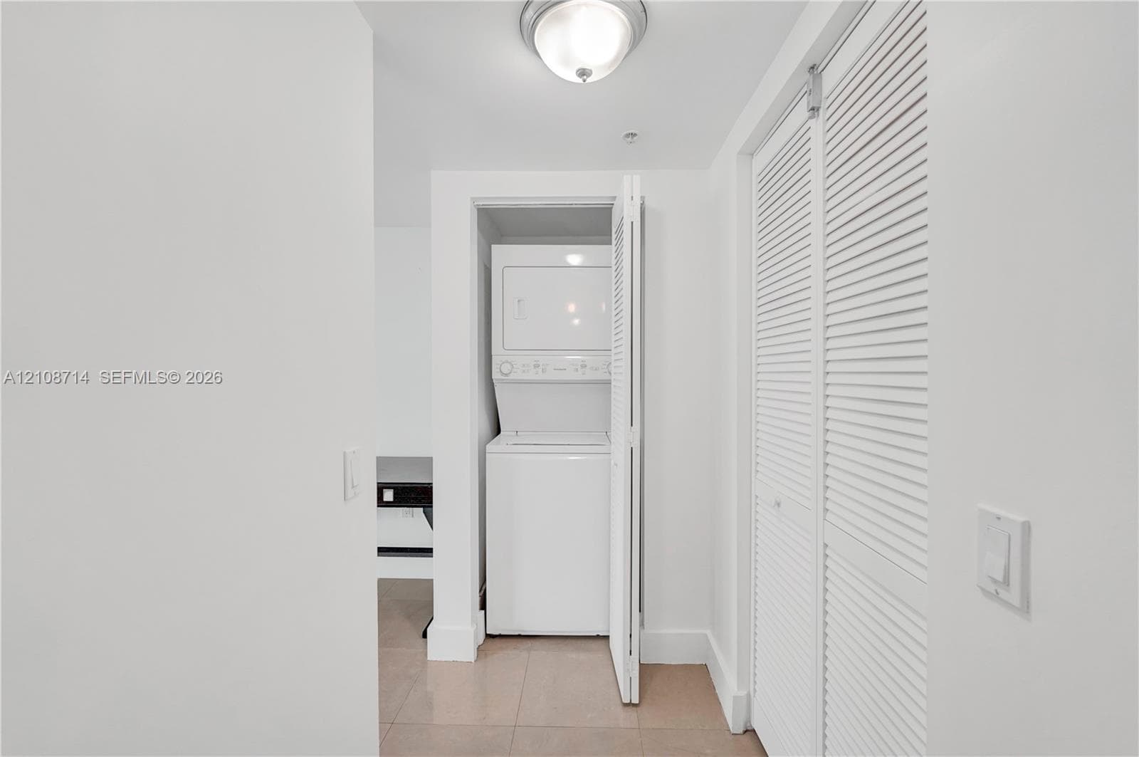 Stacked laundry unit, louvered closet doors, and flush-mount overhead lighting